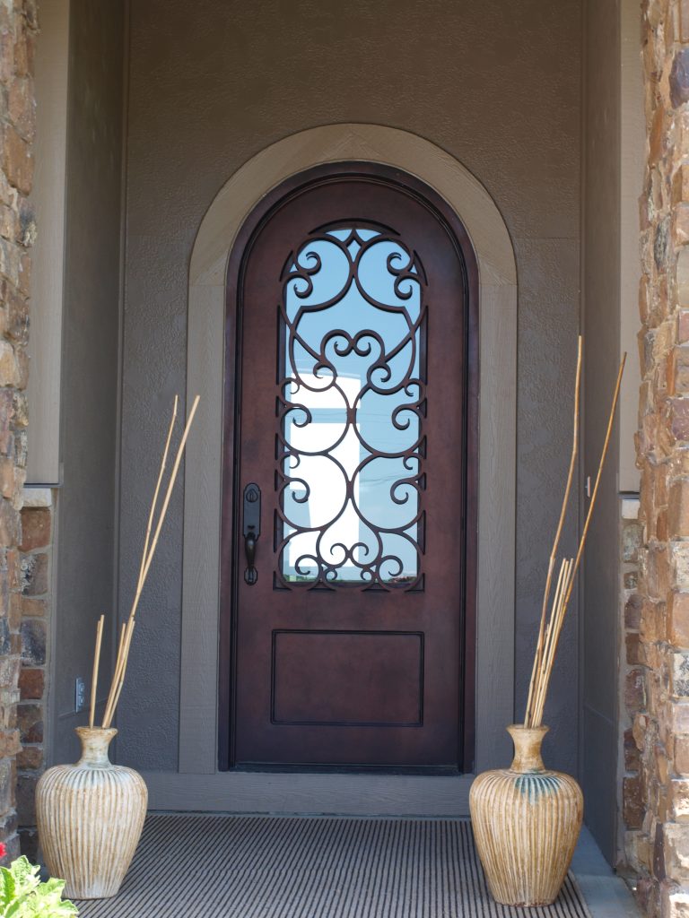 Round top iron door installed in entryway with decorative pots